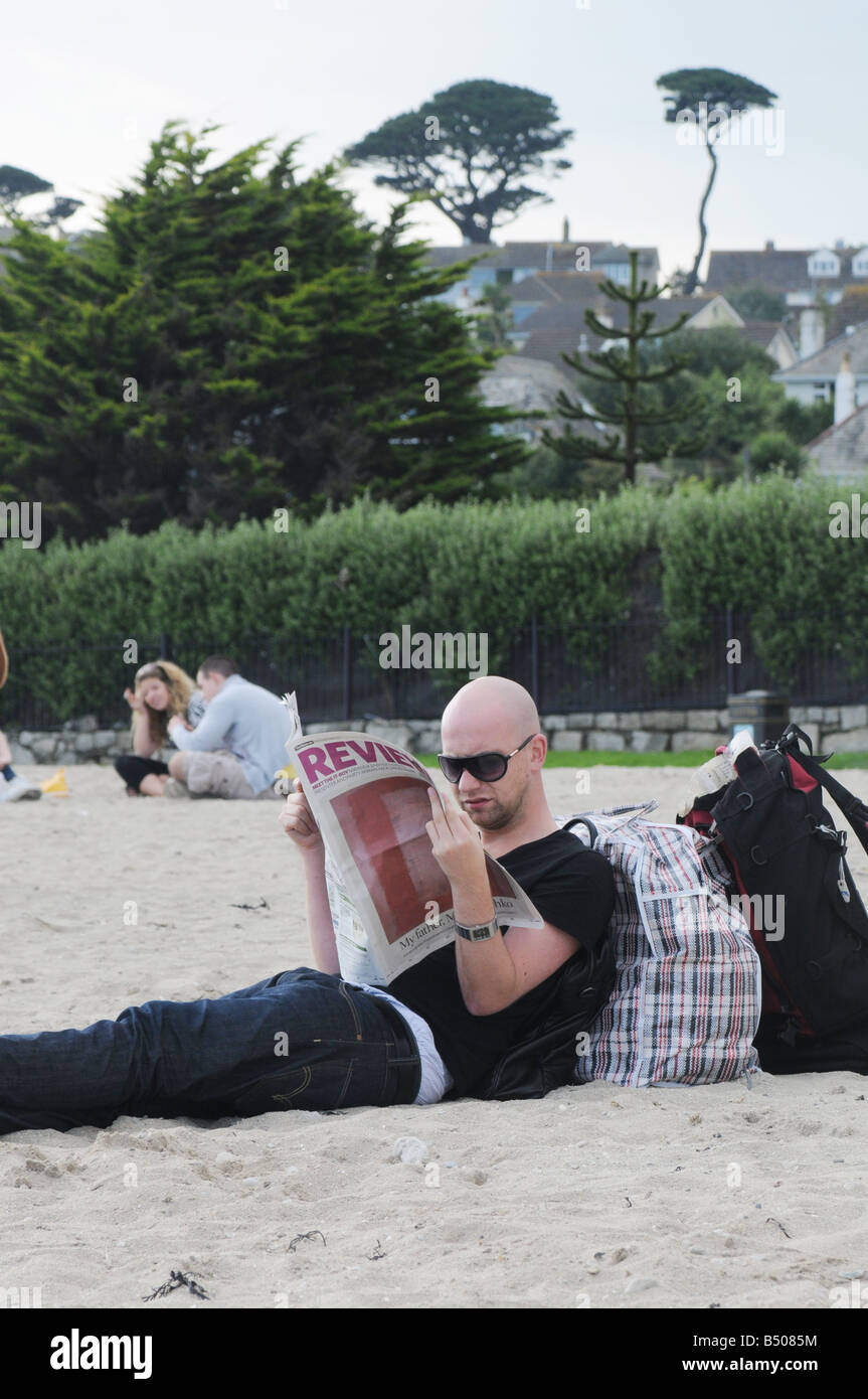 Un giovane uomo che legge il giornale inglese The Guardian su una spiaggia in Cornwall, Regno Unito Foto Stock