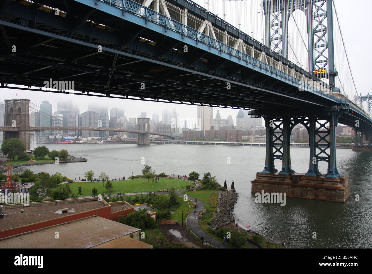 Manhattan Bridge incornicia il Ponte di Brooklyn e Manhattan sullo sfondo. In primo piano si trova l'Empire Fulton Ferry Park, Brooklyn, New York City. Foto Stock