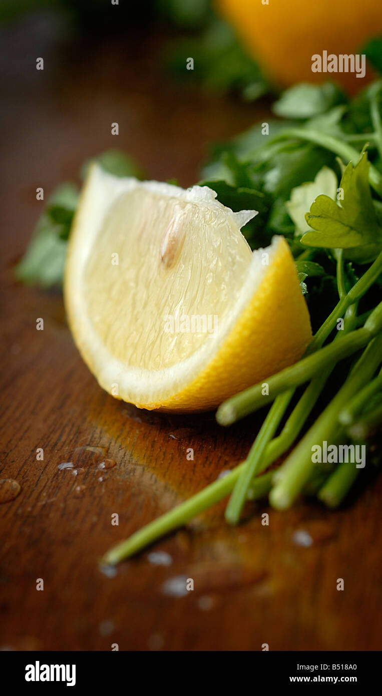 Il cibo della fotografia stock - una fetta di limone e il mazzetto di prezzemolo a foglia piatta al buio su un tavolo di legno. Foto Stock