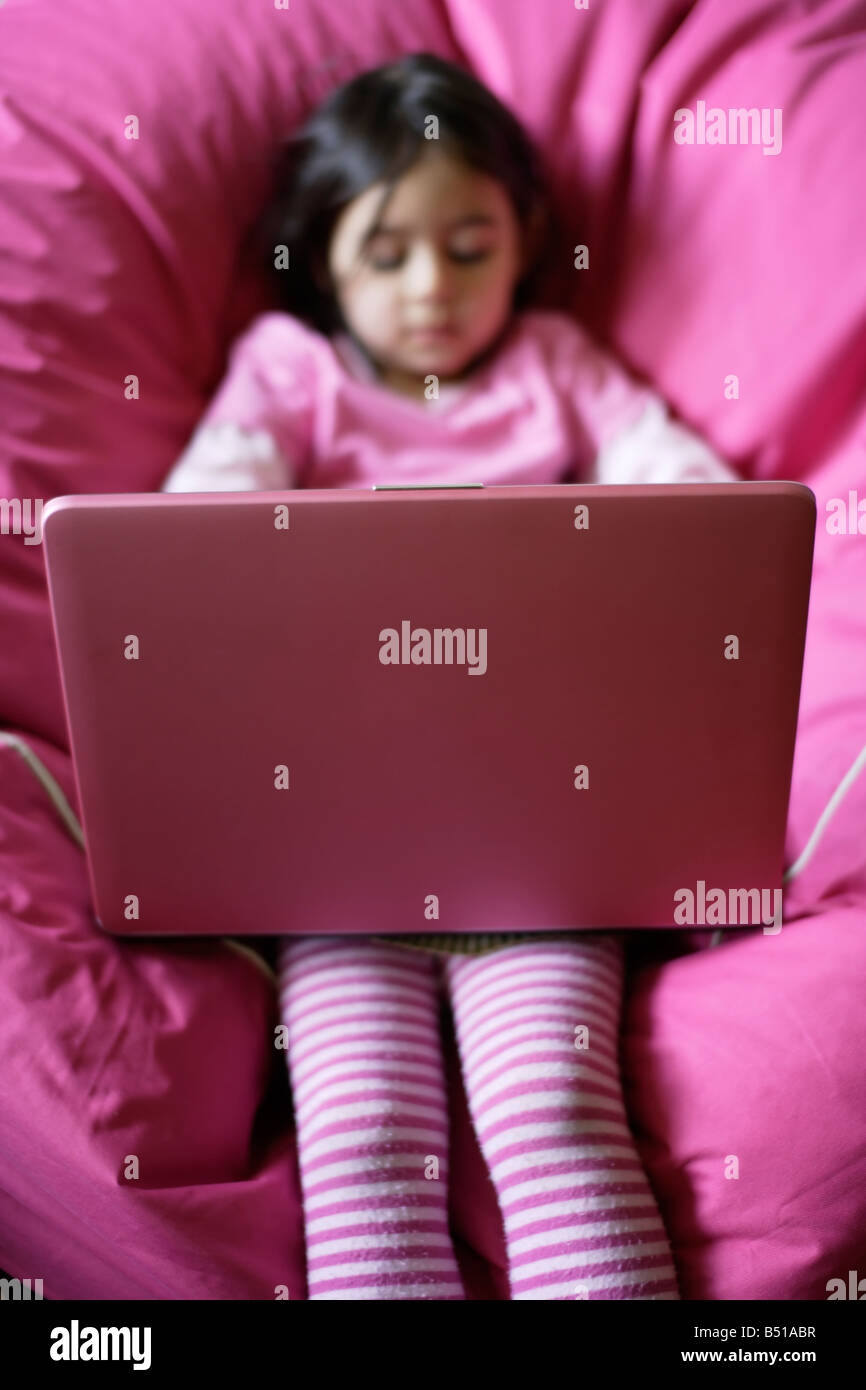 Bambina di cinque anni con rosa computer portatile seduto su beanbag rosa Foto Stock