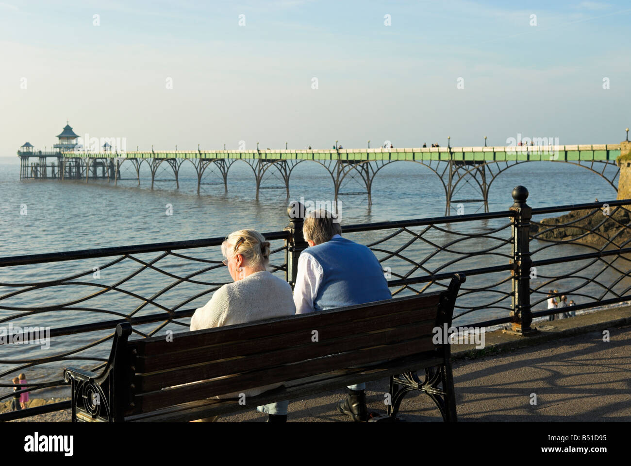 Anziana coppia seduta sul banco Clevedon lungomare affacciato sulla spiaggia e molo nord Somerset England Regno Unito Foto Stock