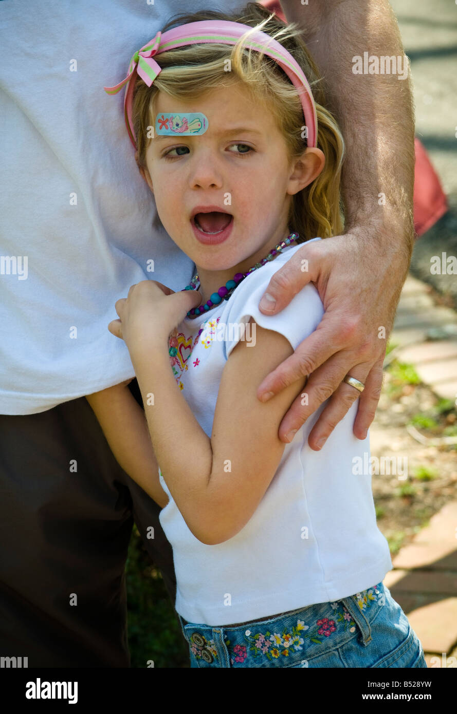 Ragazza giovane trova conforto in sicurezza nelle braccia del padre. Banda colorata aiuto sul fronte Foto Stock