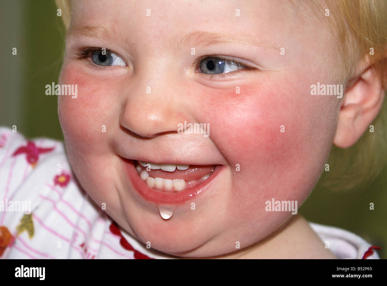 Closeup ritratto di sorridere blue-eyed blonde bambino con bava in corrispondenza del bordo del labbro isolato mediante messa a fuoco selezionata Foto Stock