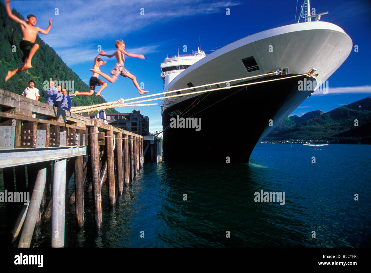 I bambini di saltare fuori di un dock commerciale in acqua con una nave da crociera ormeggiata vicino in Juneau Alaska durante l'estate Foto Stock