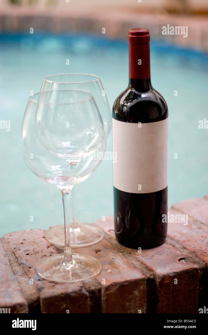 Un vino rosso bottiglia e due bicchieri vuoti dal pool abbondanza di spazio copia sul vuoto etichetta del vino Foto Stock