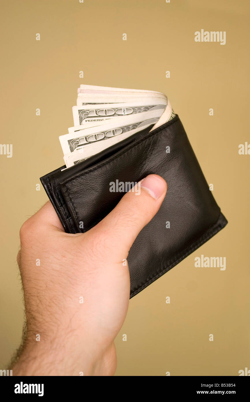 Una mano che tiene un portafoglio pieno di contanti isolate su un fondo dorato Foto Stock
