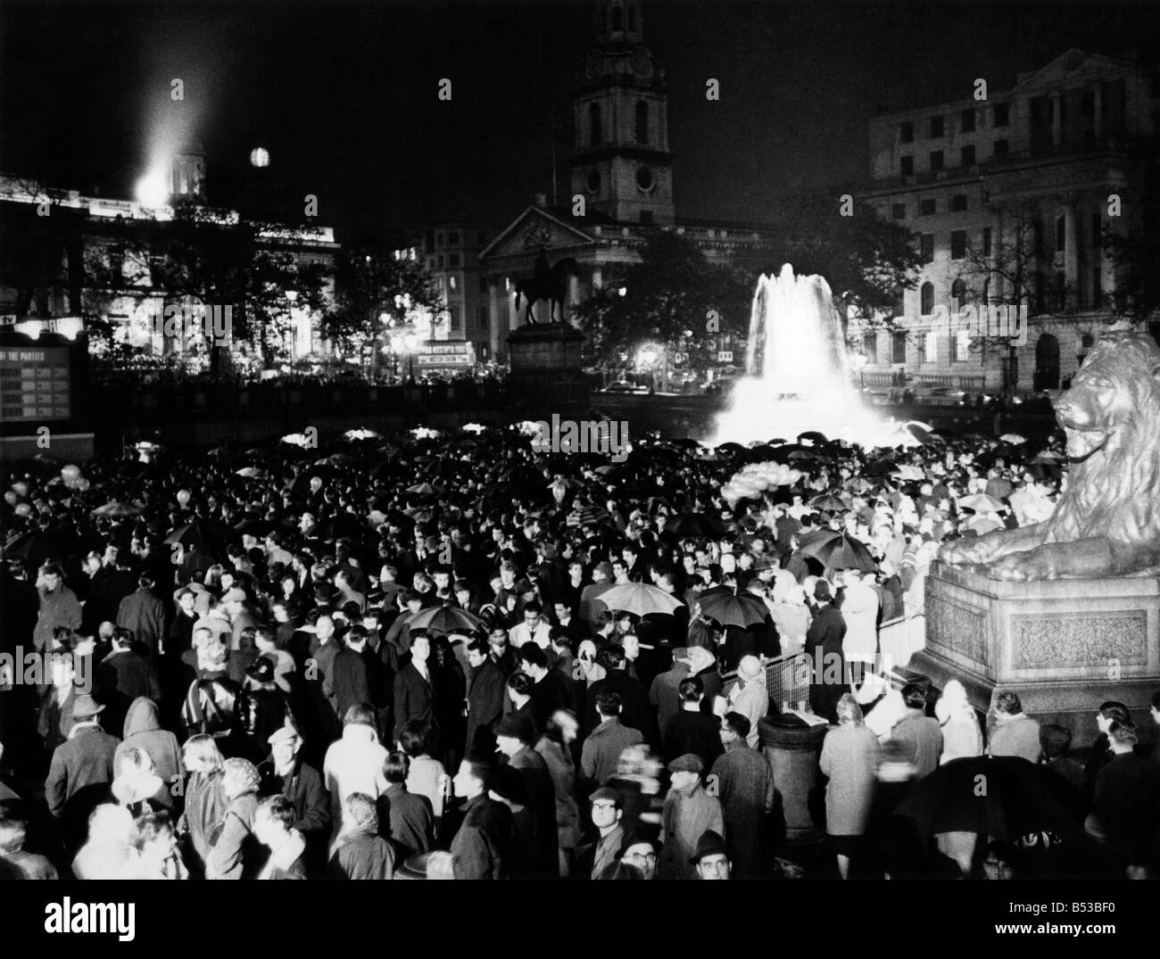 Cheers sotto la pioggia. Migliaia inceppata a Trafalgar square come la pioggia versata all ultima notte (giovedì 15-10-64) e, in vista del Parlamento, guardato le parti in lotta per il controllo del paese. Essi allietate, booed cantato - e alcuni di essi anche saltato nella fontana piscine in loro entusiasmo - come i risultati delle elezioni sono stati riprogrammati per la folla ogni pochi istanti su un grande schermo televisivo. Ottobre 1964 ;P018731 Foto Stock