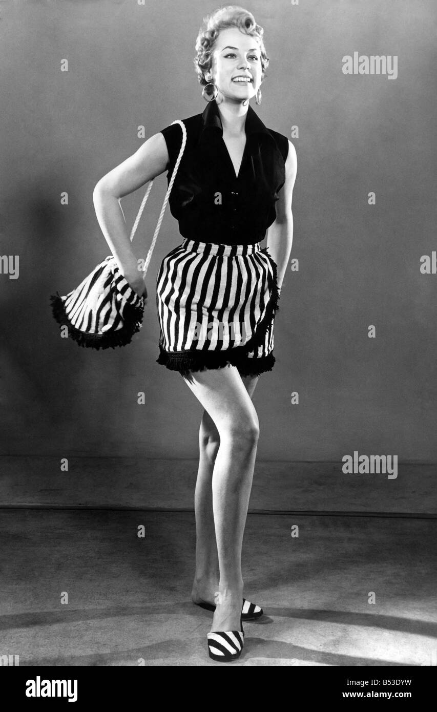 Donna vestite per aday presso la spiaggia, indossando sleveless top e gonna a strisce, portando un abbinamento borsetta. Aprile 1954 Foto Stock