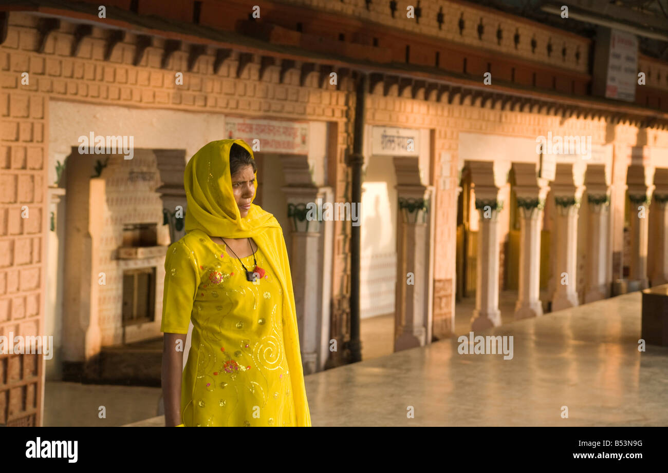 Una donna passeggero in un sari giallo in attesa sulla piattaforma, Sawai Madhopur stazione, Rajasthan, India Foto Stock
