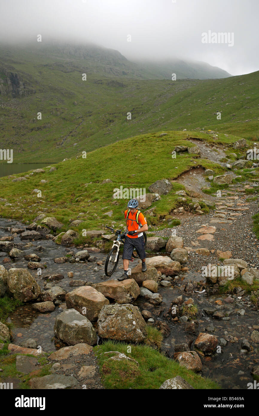 Mountain Biker attraversa un ruscello di montagna nel distretto del Lago Foto Stock