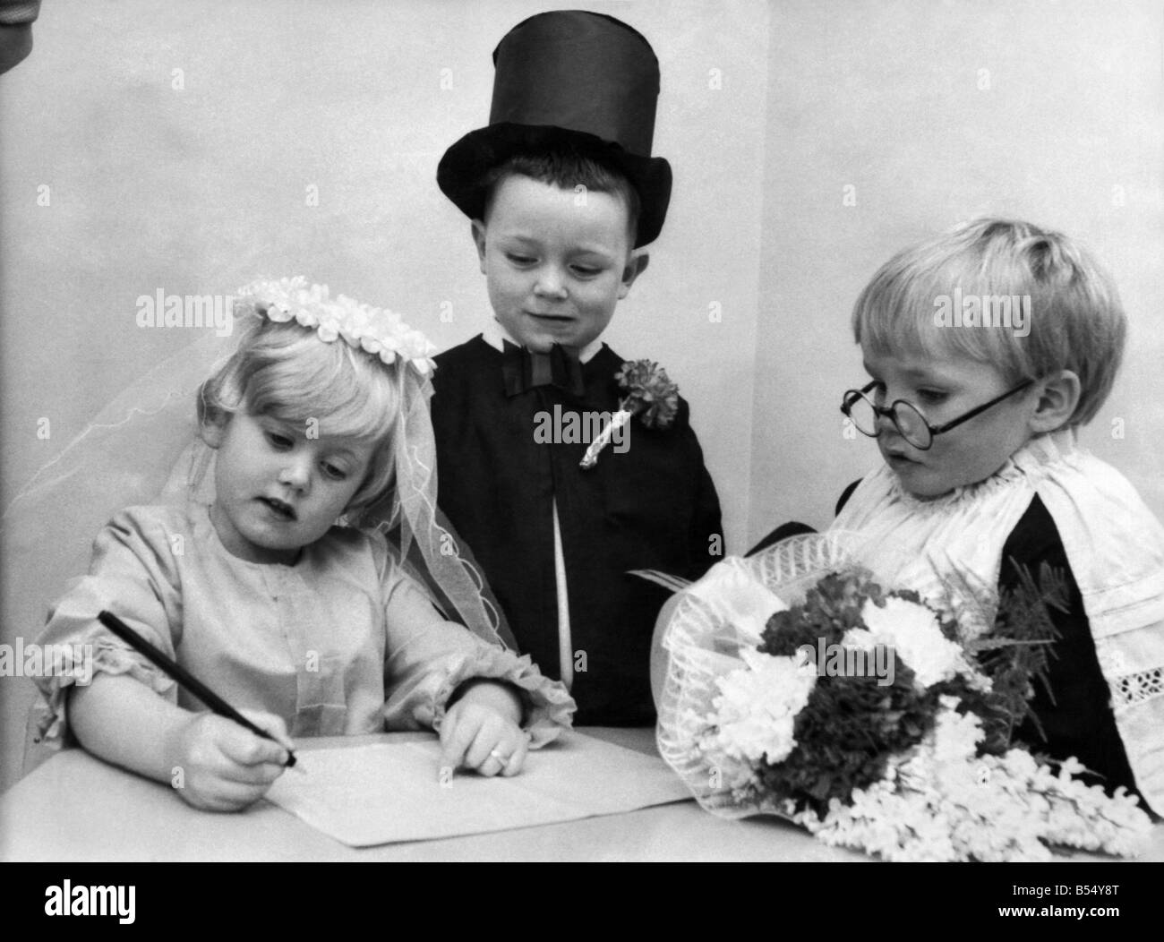 Tiny Tots a Bluebell Vivaio a Huyton, Liverpool, ha preso parte a una simulazione di cerimonia nuziale di ieri. Sposa Helen Smith, 4, e sposo, Ian Welsh, 4, faccia il vicario Stewart Fergie, 4, come si sono sposati a modificare. Coppia giovane firmare il registro. Marzo 1970 P12091 Foto Stock