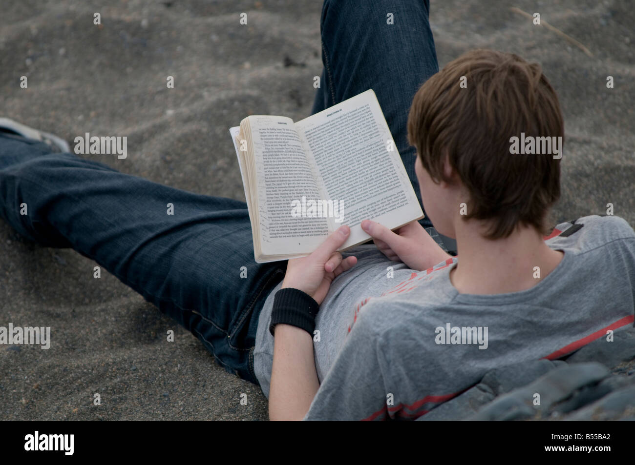 Giovane uomo Aberystwyth studente universitario la lettura di libro in brossura sulla spiaggia Foto Stock