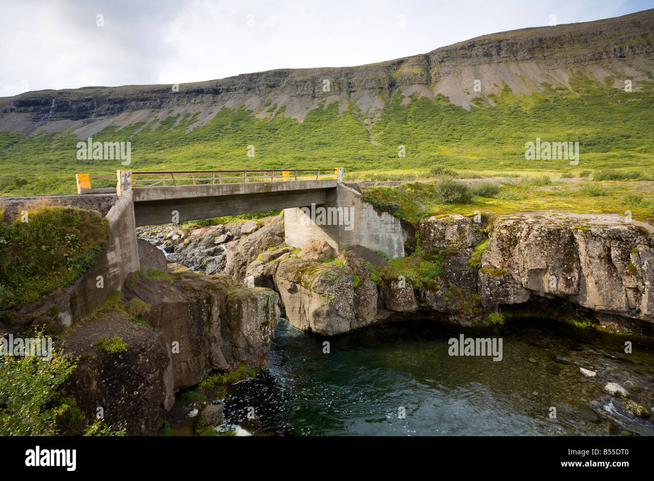 Singola corsia ponte che attraversa un ruscello con Sunnfjall in background Westfjords Islanda Foto Stock