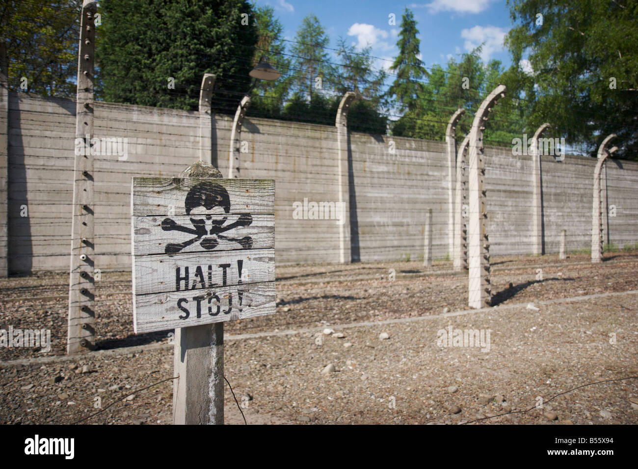 Segnale di avviso con le ossa craniche simbolo nella parte anteriore del filo spinato recinzione elettrificata e un muro di cemento in Auschwitz I Foto Stock