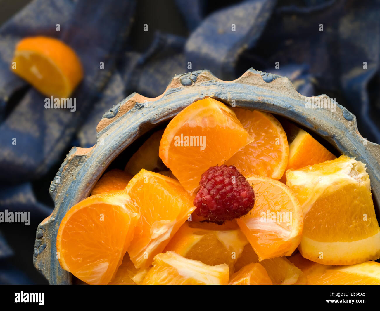 Una ciotola di fettine di arance e un lampone su uno sfondo sfocato, con una fetta di arancio in blur Foto Stock