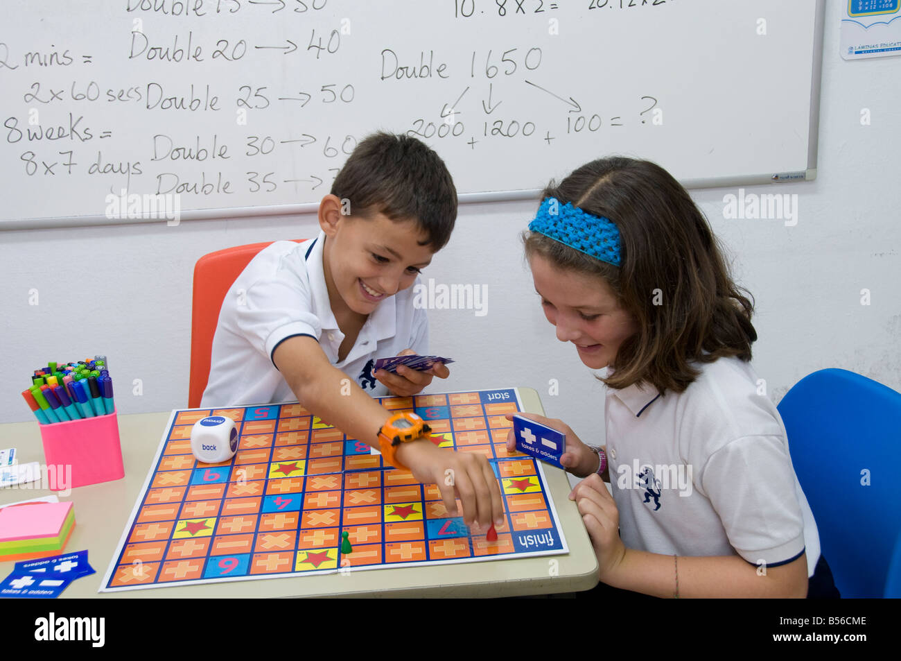 Scuola Junior i bambini in Aula la riproduzione di un matematico competitivo gioco di bordo di aggiunta di ,la sottrazione e la moltiplicazione. Foto Stock