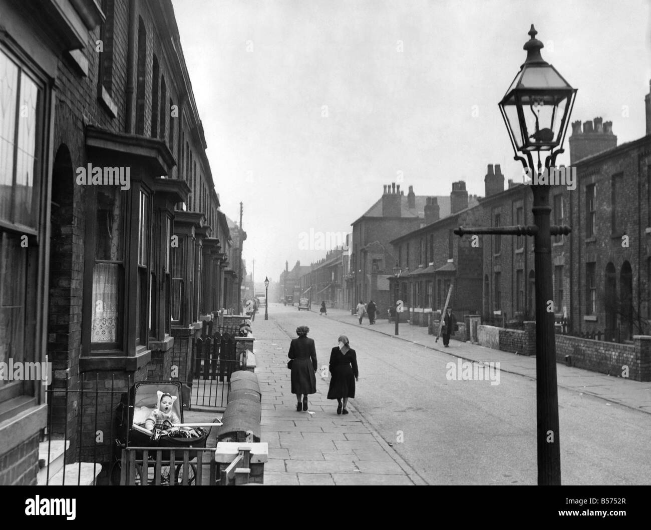 Un bambino si siede nella sua pram al di fuori della parte anteriore di una casa in una strada appartata, in Cheetham Hill area di Manchester. Marzo 1953 Foto Stock