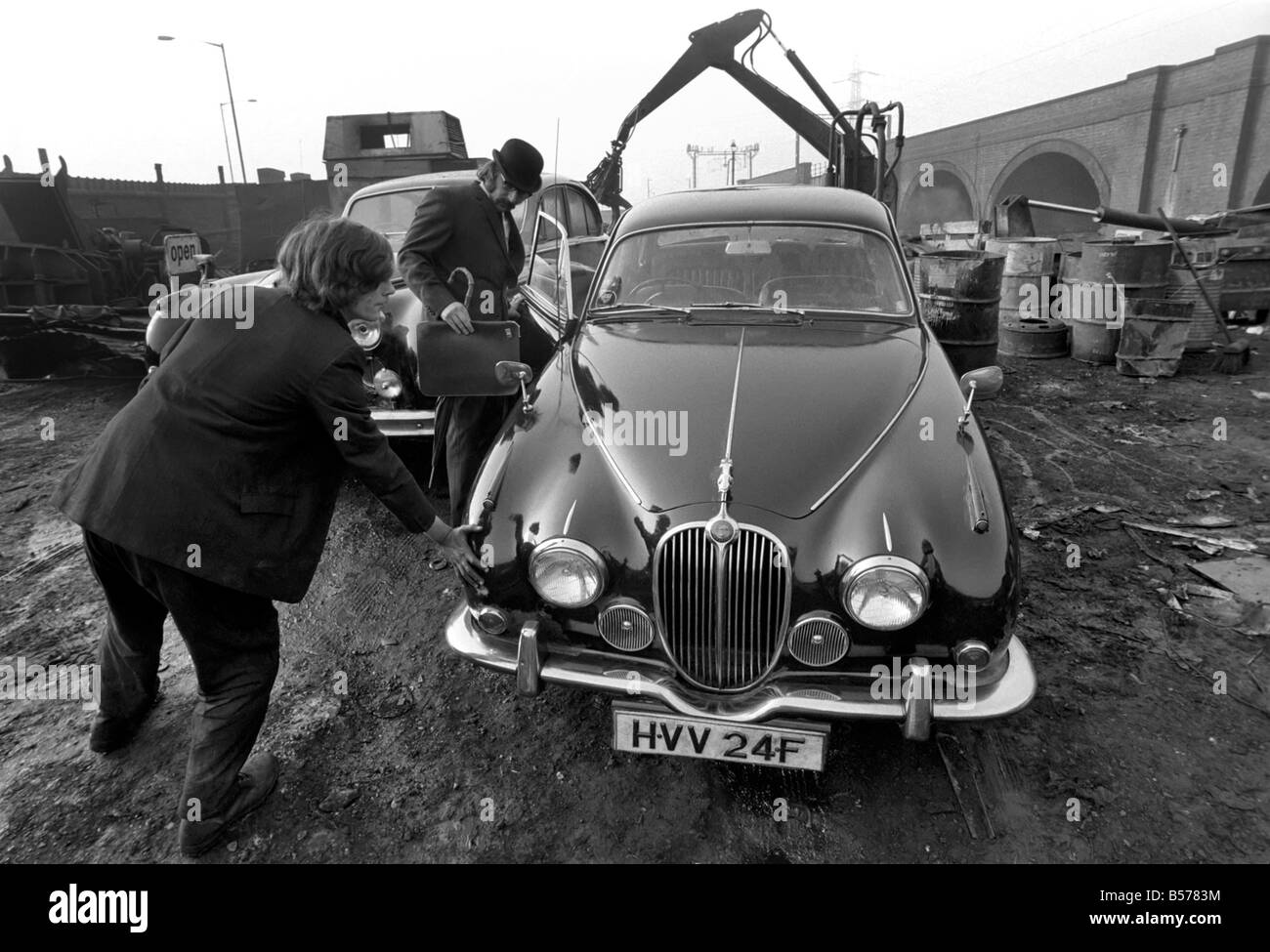 Insolito/Suit/Bowler cappello: Uomo sfridi Jaguar auto: D'altro canto, direttore delle vendite per il sig. Graham Parkes, chi dice che non può più permettersi di eseguire il suo 15 miglia per gallone Jaguar, e era disgustato presso i concessionari' offre, ha deciso di guardare la sua distruzione. Febbraio 1975 75-01164-002 Foto Stock