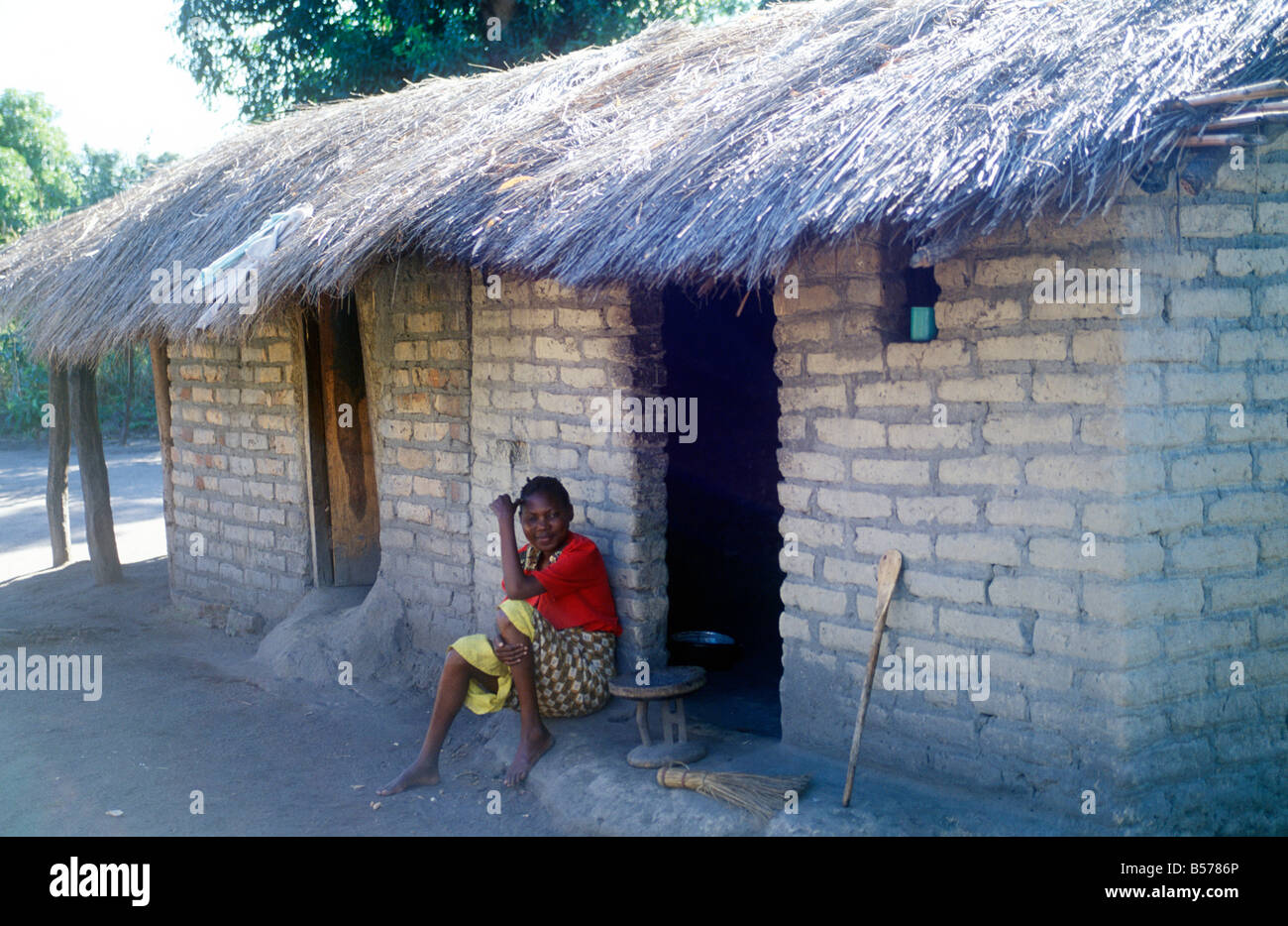 Una donna seduta accanto alla sua casa di paglia in un villaggio vicino a Spiaggia di Kande, il Lago Malawi, Africa Foto Stock