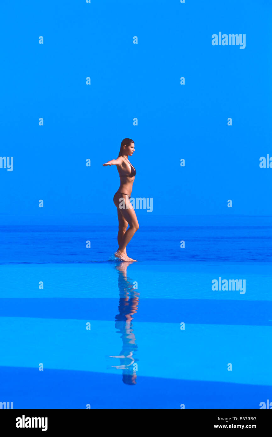 Donna che cammina sul bordo della piscina a sfioro, Maldive, Oceano Indiano, Asia Foto Stock