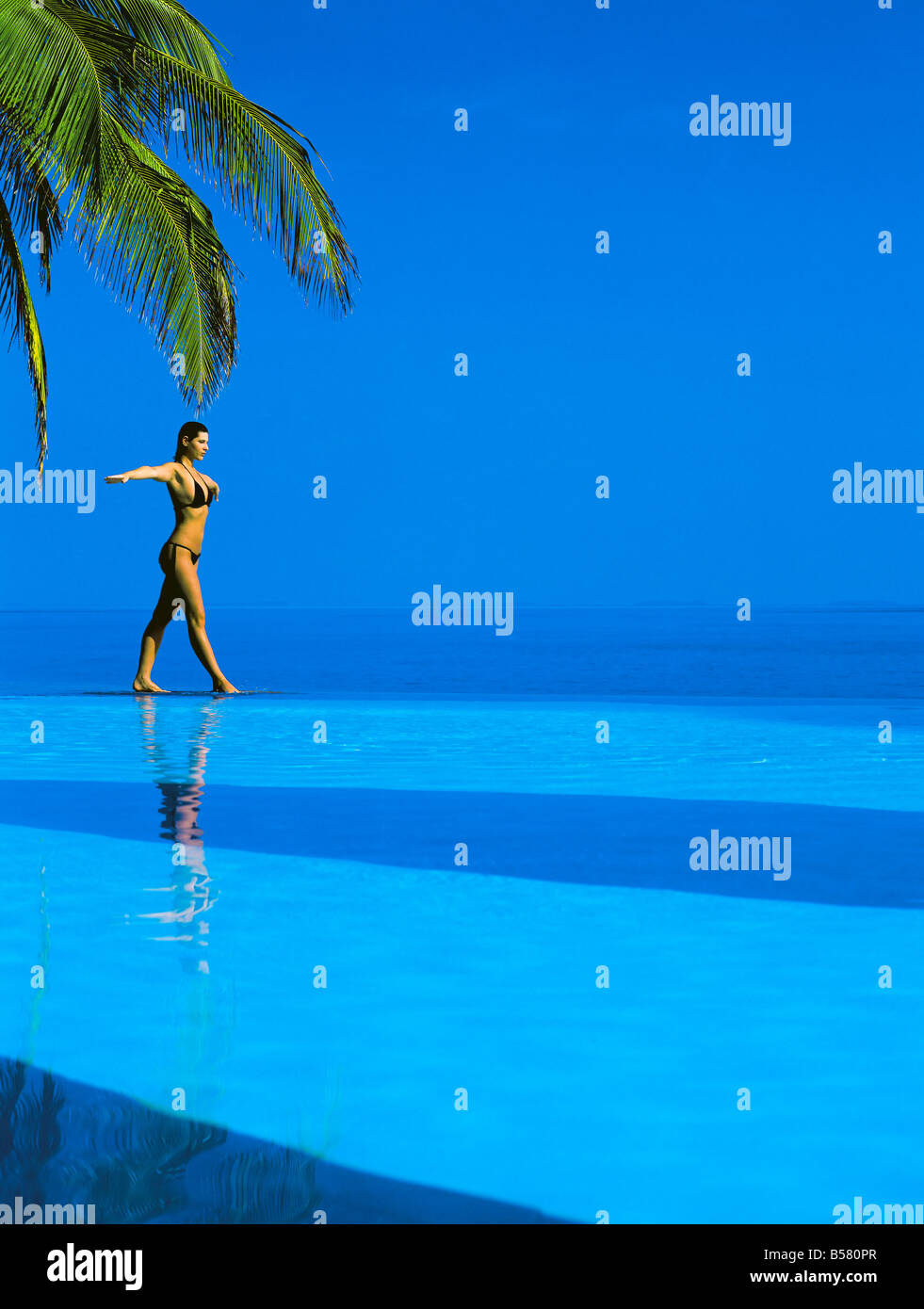 Bilanciamento della donna sul bordo della piscina a sfioro, Maldive, Oceano Indiano, Asia Foto Stock