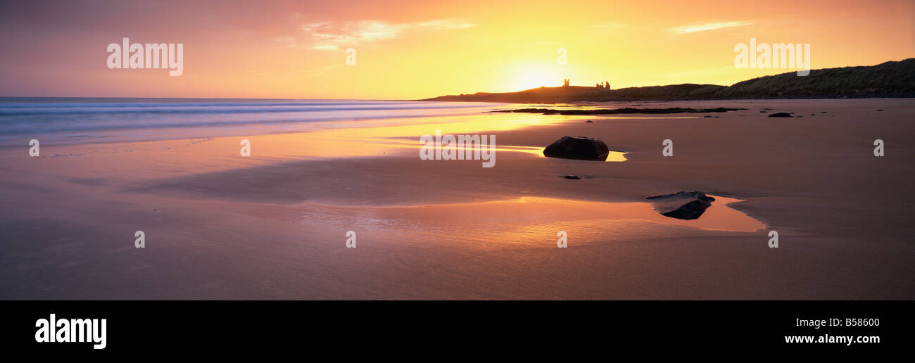 Vista lungo Embleton Bay all'alba, con silhouette di Dunstanburgh Castle in distanza, Northumberland, Inghilterra Foto Stock