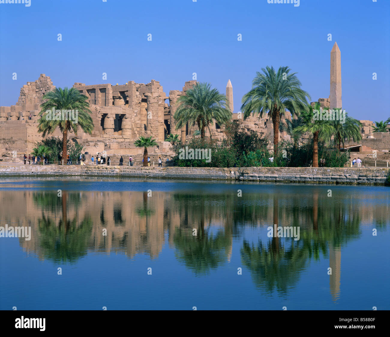 Riflessi nel lago sacro del tempio, obelischi e palme a Karnak, nei pressi di Luxor, Tebe, Egitto Foto Stock