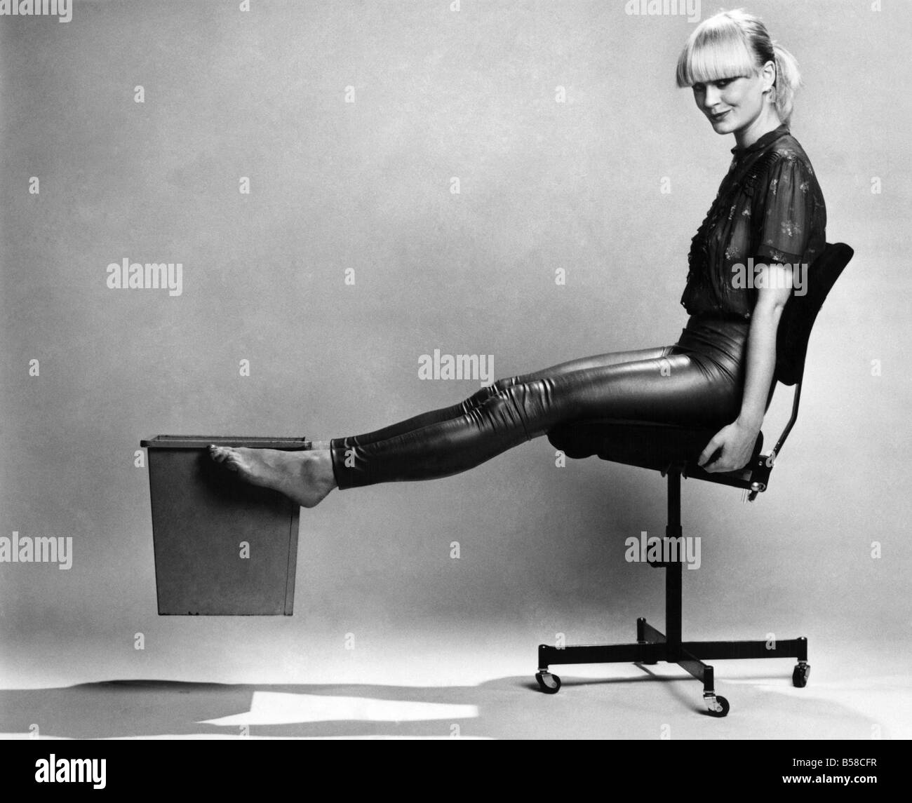 Whittles la cintura:- mettere il cestino per la carta sul pavimento davanti ai vostri piedi. Raddrizzate le gambe e cesto di attesa tra i piedi. Tenere i lati della sedia per il supporto, sollevare il cestello il più possibile vicini al livello della vita, quindi abbassare a terra. Ripetere 15 volte. Questo esercizio è eccellente per addome e girovita. Luglio 1979 P006551 Foto Stock