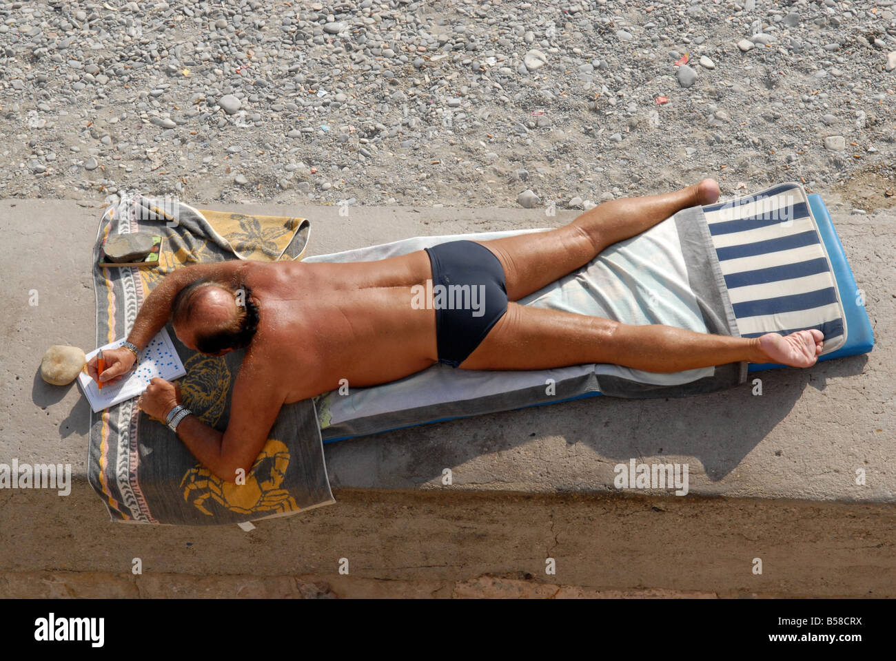 L'uomo rilassante in vacanza facendo il cruciverba sulla spiaggia Foto Stock