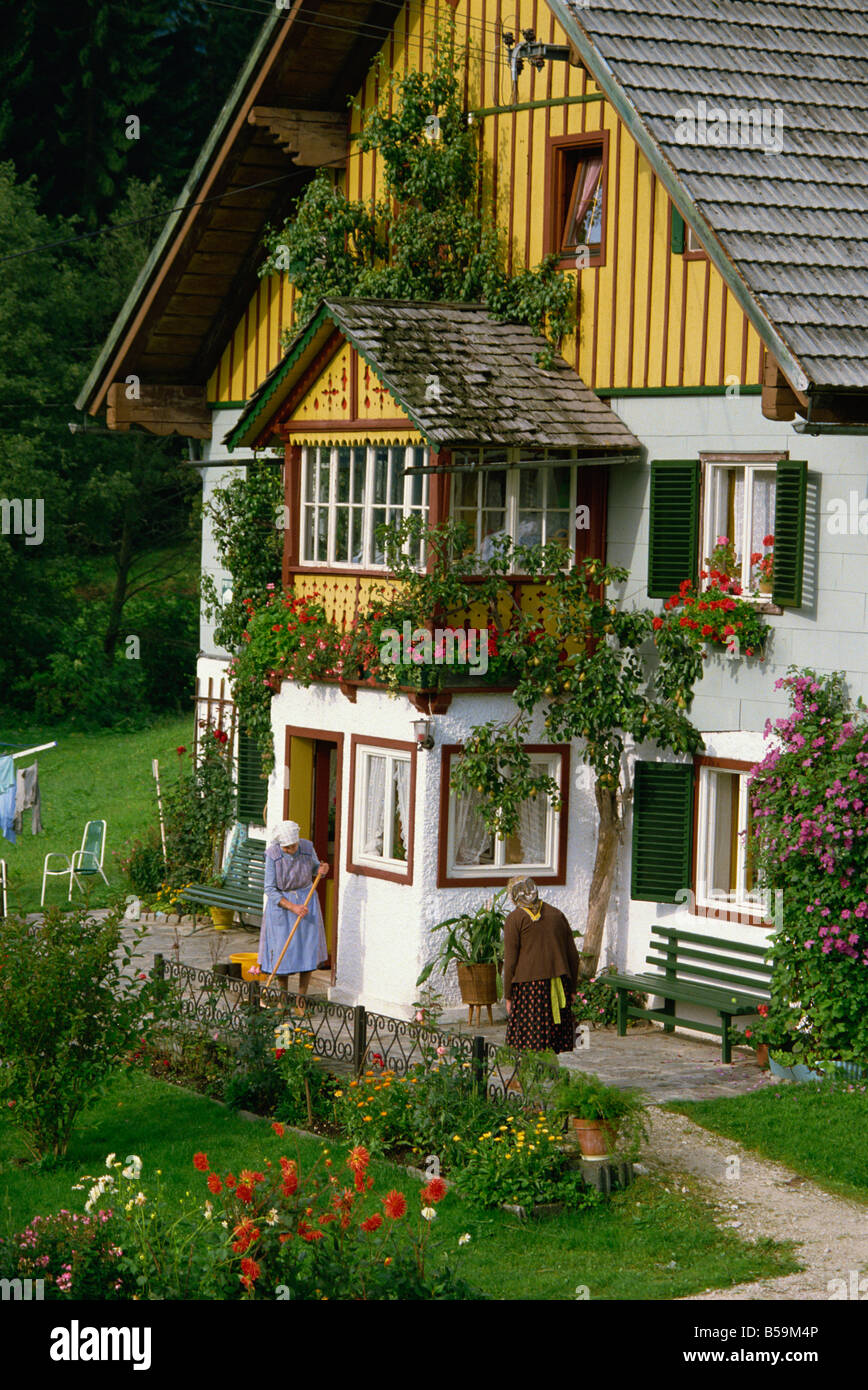 Due signore al di fuori di una casa tipica con fiori estivi in windowboxes e nel giardino, nell'area Salzkammergut dell'Austria Foto Stock