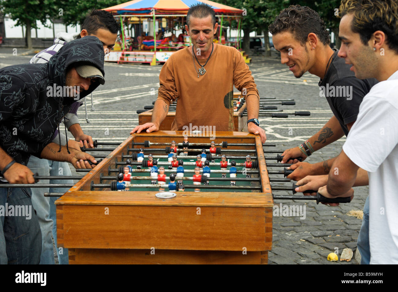Quattro giovani uomini a giocare "calcio" nel parco all'aperto con un altro a guardare Foto Stock