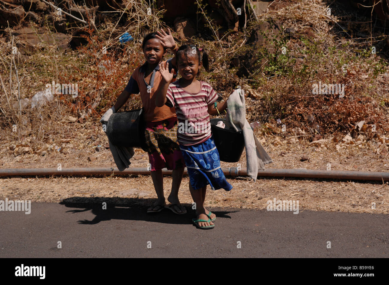 Bambini Balinese con cestello sventolare le loro mani a turistica mentre si cammina lungo la strada per andare sotto la doccia,Bali, Indonesia. Foto Stock