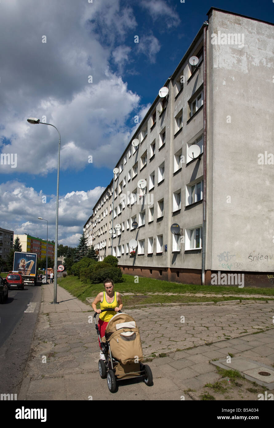 Donna spingendo la PRAM sulla strada trafficata passato blocco di cemento appartamenti Miastko Polonia Foto Stock