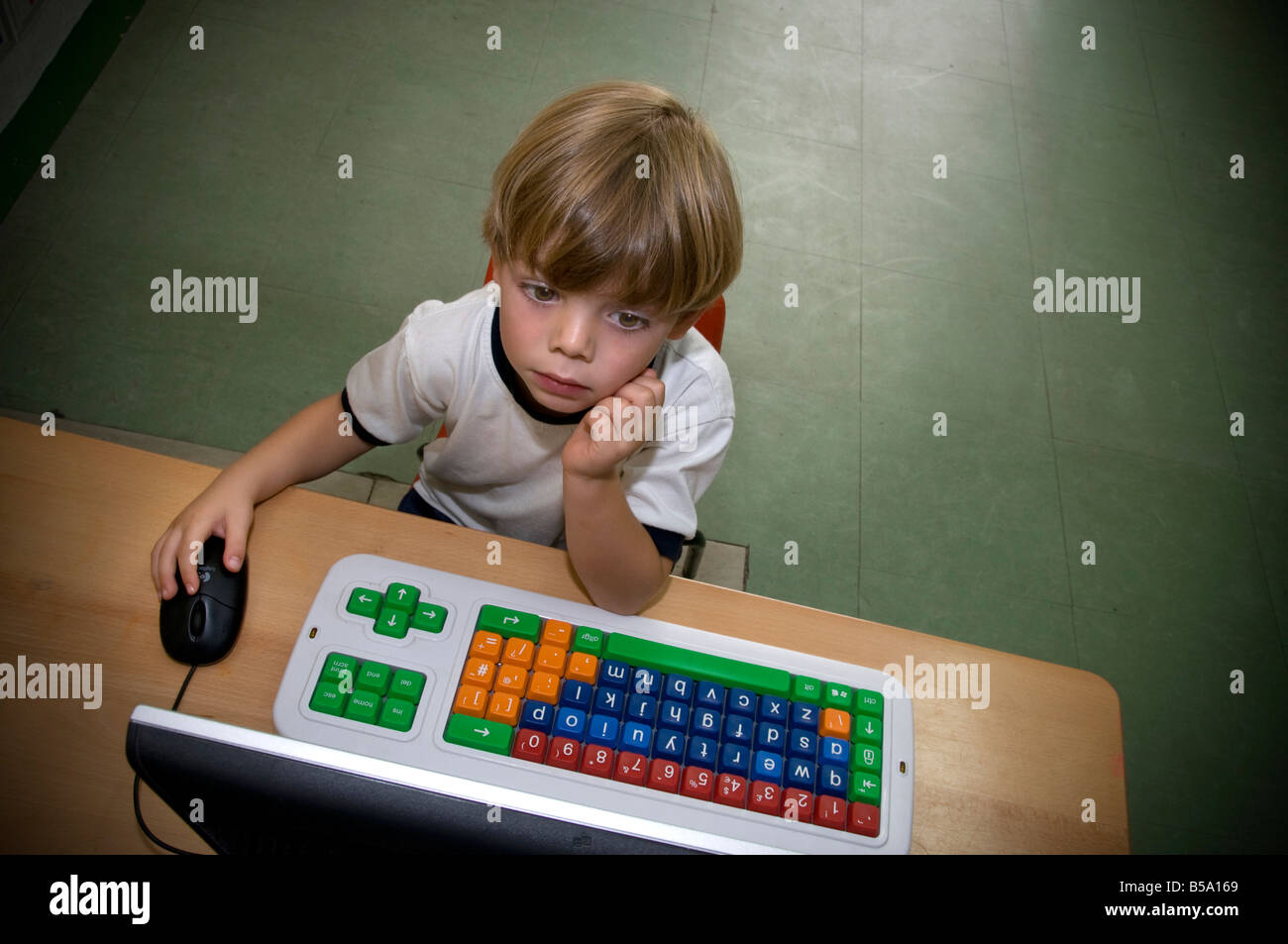 Asilo Infantile computer boy 4-6 anni intensamente gli studi presso la sua speciale con codice colore kindergarten scuola di computer e mouse in classe solo camera Foto Stock