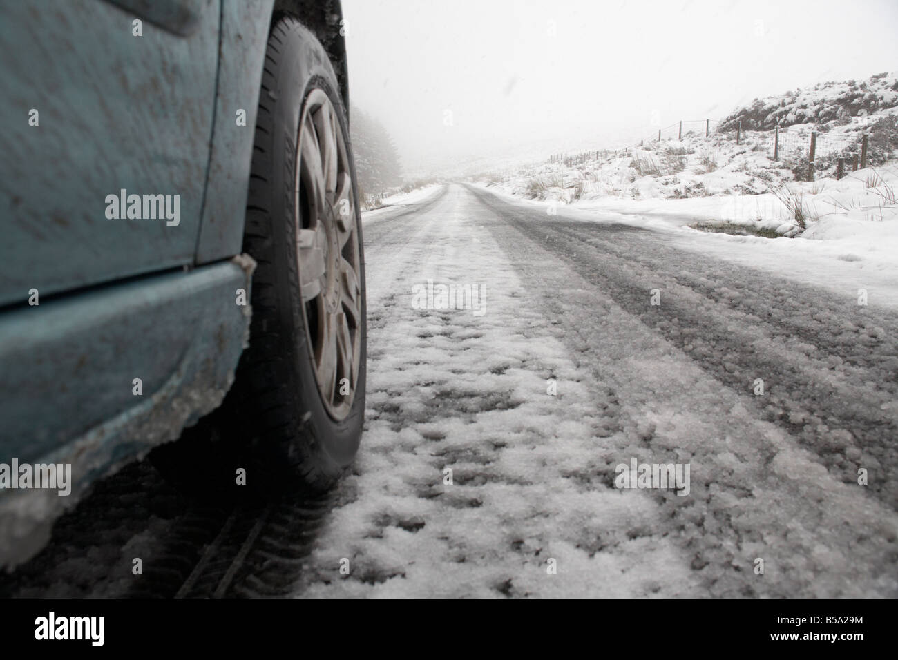 Auto ruota e la neve e il ghiaccio su un telecomando rurale di strada di montagna in esecuzione passato una foresta nella contea di Antrim Irlanda del Nord Regno Unito Foto Stock