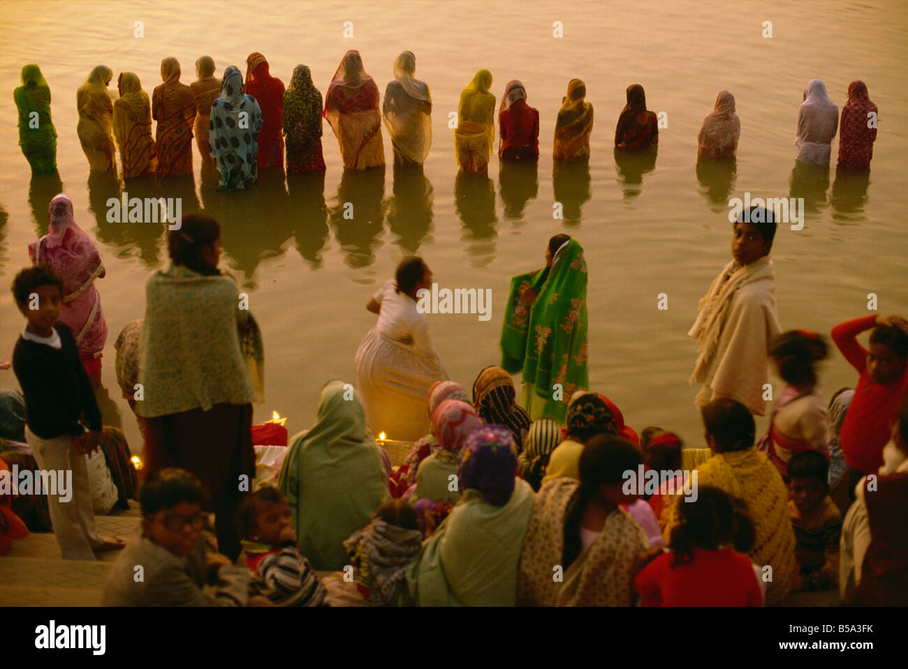 Le donne si raccolgono lungo il fronte fiume, ad accogliere il Rising Sun dio, Surya, adorare il sole Festival, Varanasi, nello stato di Uttar Pradesh, India Foto Stock