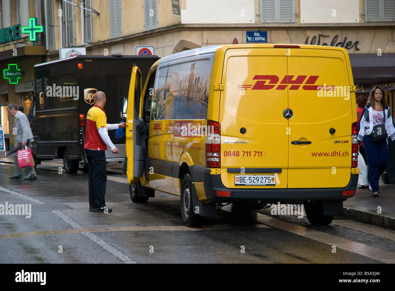 Un dhl delivery conducente sorge nella strada guardando un carrello Foto Stock