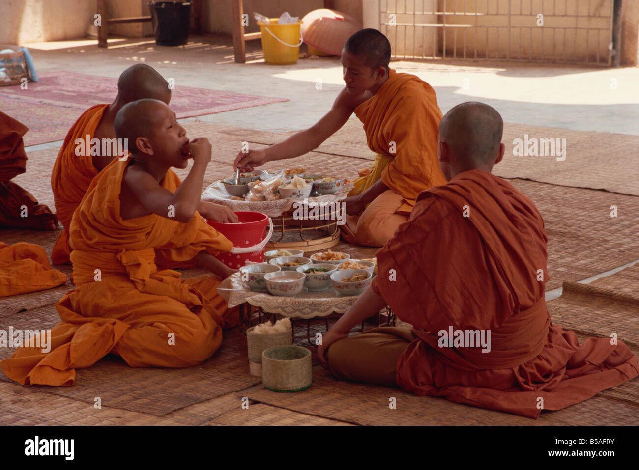 I monaci in abiti dello zafferano seduta sul pavimento a mangiare wat Chan in Vientiane Laos Asia L TAYLOR Foto Stock