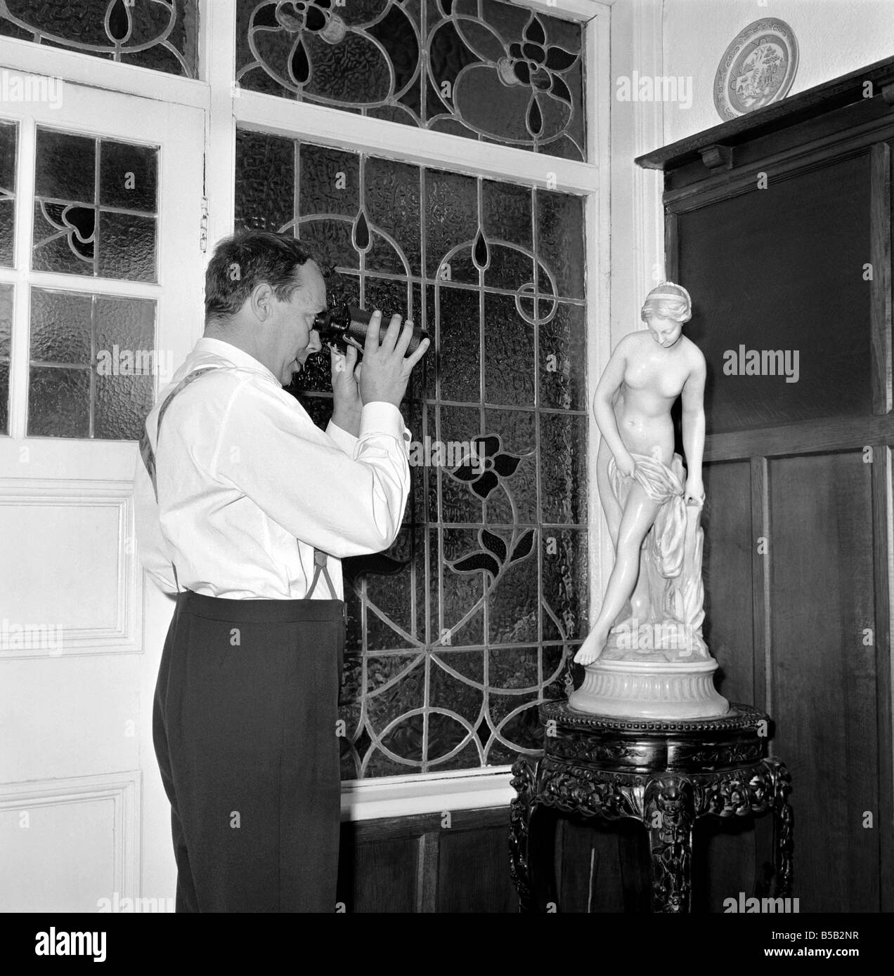 Eric Morecambe visto qui a casa guardando la statua attraverso binoculers. 1963 Foto Stock