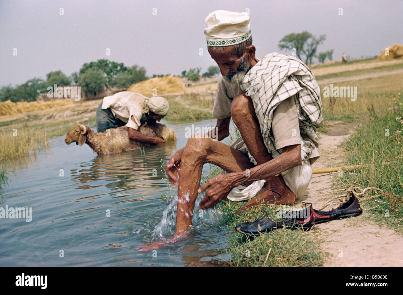 Due uomini anziani lavaggio in un fosso di irrigazione in un villaggio nel Punjab Pakistan Asia R Ashworth Foto Stock