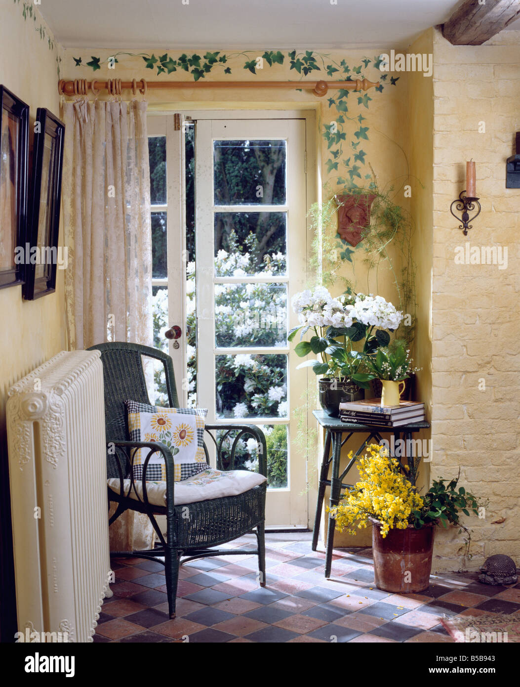 Impresse foglie d'edera sopra le porte Francesi con crema tenda nella hall con la vecchia cava pavimento piastrellato e una sedia di vimini accanto al radiatore Foto Stock