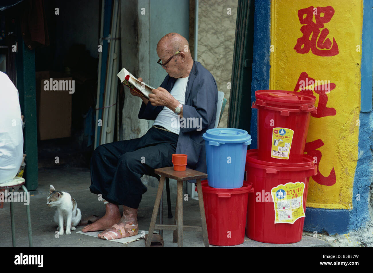 Uomo anziano con piede bendato, indossa gli occhiali e la lettura di un libro, Singapore Foto Stock