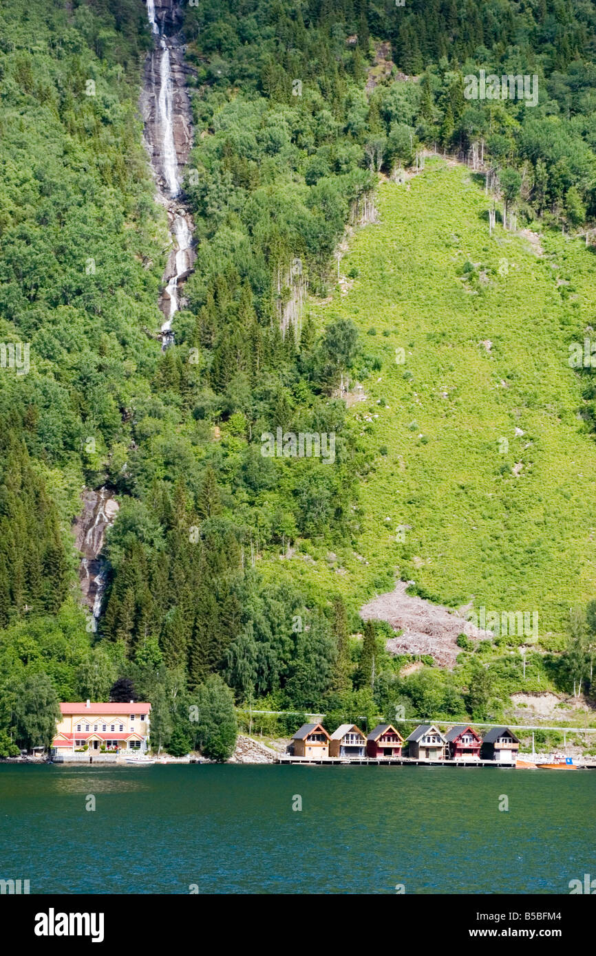 Linea Boathouses l'acqua e una cascata precipita da sopra il fiordo Sognefjord in Norvegia. Foto Stock