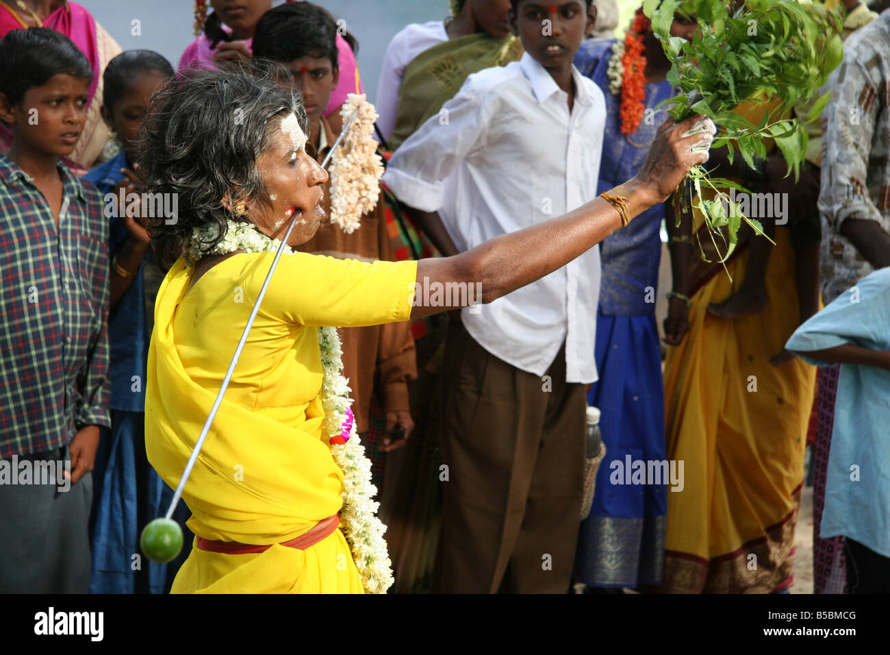 Una donna cammina attraverso un villaggio rurale in Tamil Nadu con un'asta di metallo attraverso le sue guance. Foto Stock