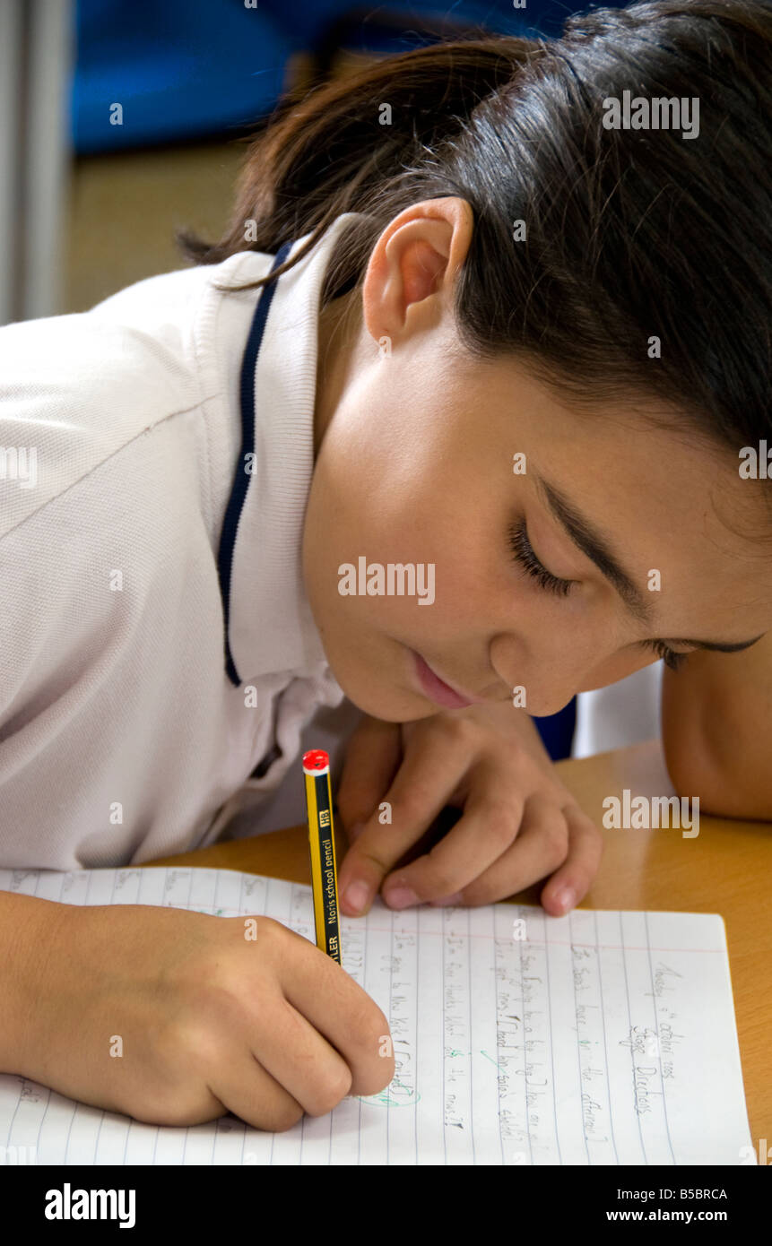 Junior schoolgirl 9-11 anni si concentra sul suo iscritto alla sua scrivania nella scuola primaria classroom Foto Stock