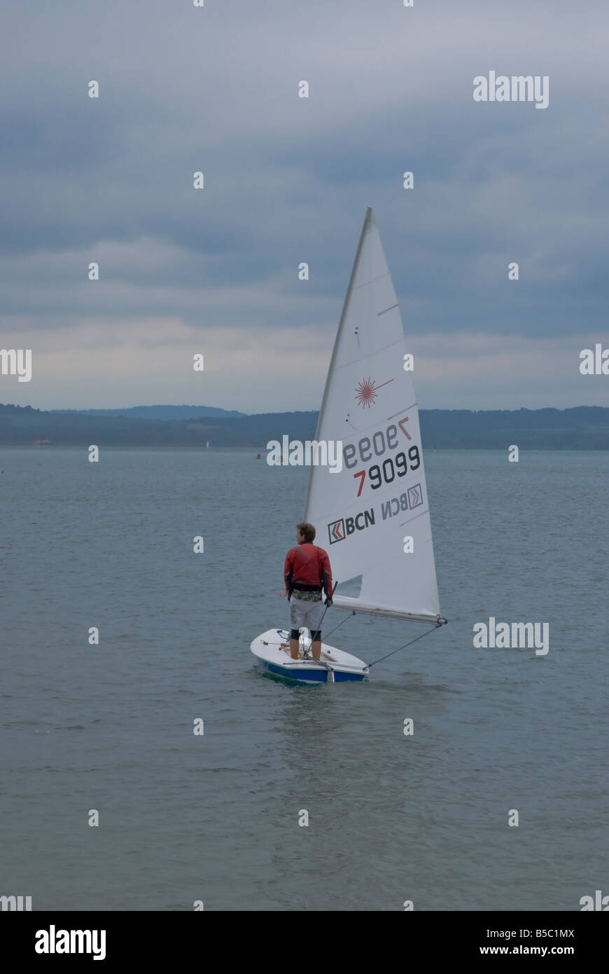 Un marinaio solitario sorge sulla sua piccola barca a vela Foto Stock