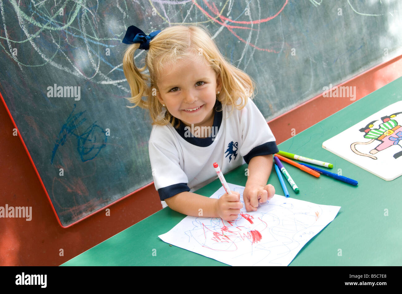 Sorridenti attraente ragazza infantile al di fuori nella soleggiata kindergarten scuola imparare a formare e disegnare forme Foto Stock