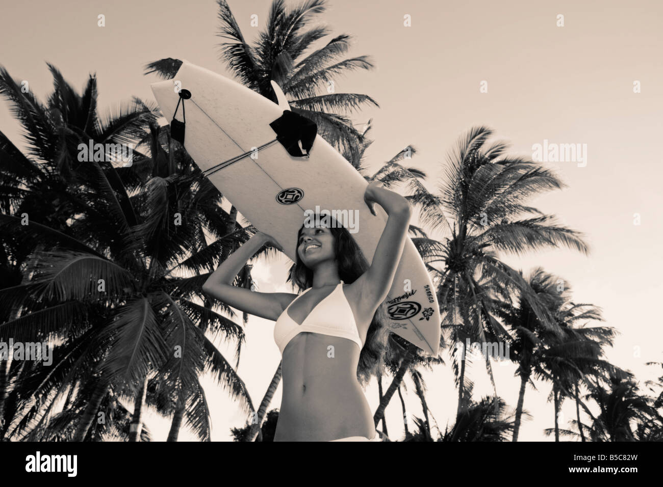 Una bella diciannovenne donna in un bikini bianco contiene una tavola da surf in Lahaina, Maui, Hawaii. Foto Stock