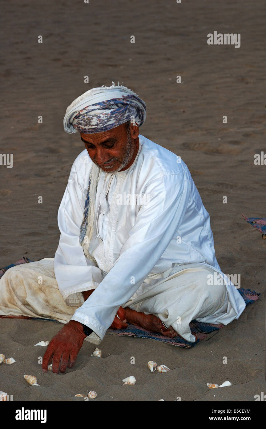 L'uomo giocando sulla spiaggia con conchiglie Hawalis, Omani variante di Mancala, Sultanato di Oman Foto Stock