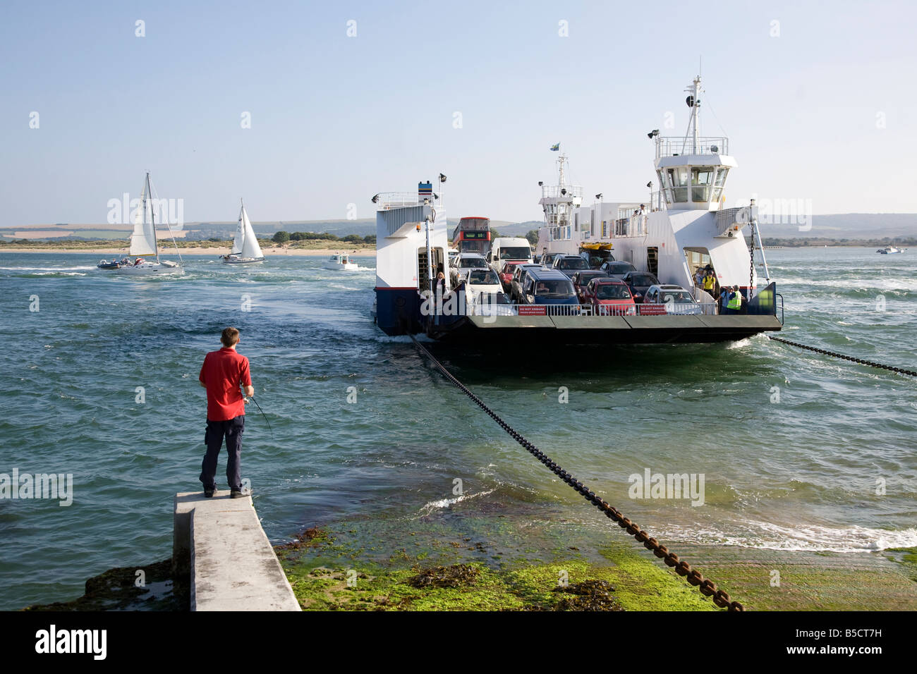 Le barene traghetto per auto Studland beach e un ragazzo di pesca presso la trafficata entrata al porto di Poole Foto Stock